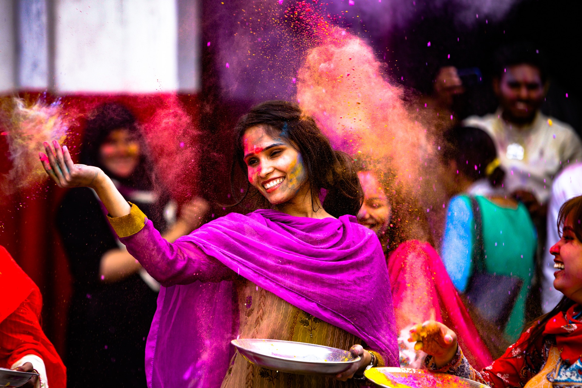 Intialainen iloinen nainen kadulla kulhokädessään heittää värijauhetta ilmaan muiden naisten kanssa.